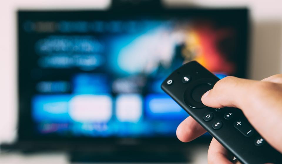 image of hand holding remote with blurred TV screen in background